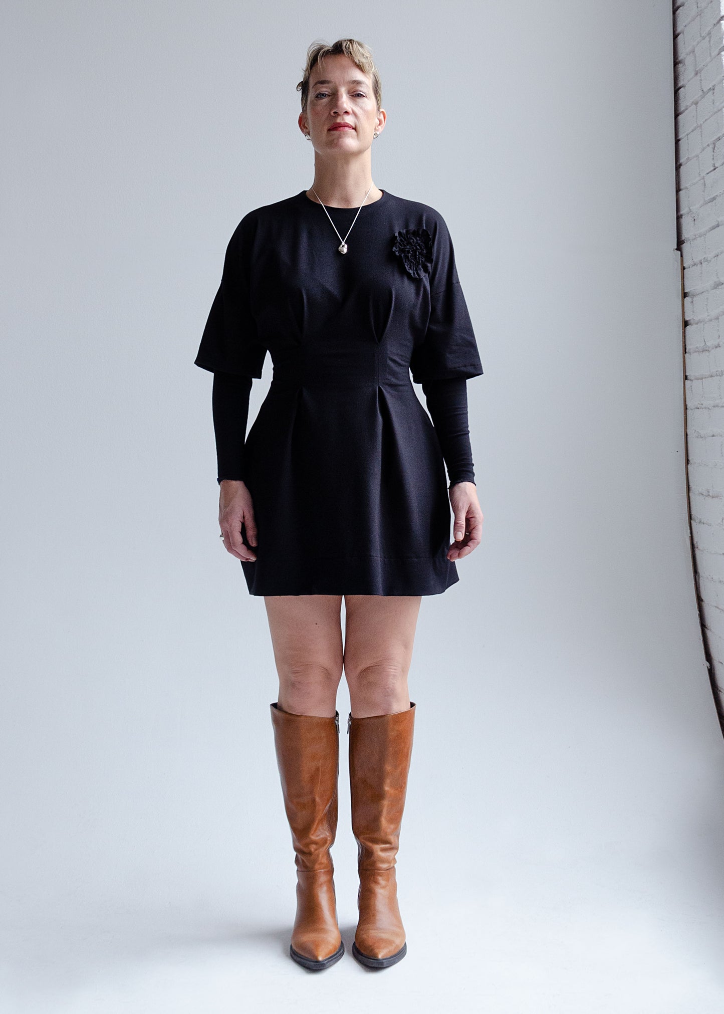 Front view, female model, drop shoulder, black knit mini dress with fit flare waist, double layer sleeve, appliqué flower detail at chest.
Cozy, stretchy cotton spandex knit jersey fabric.Our version of the "Little Black Dress"