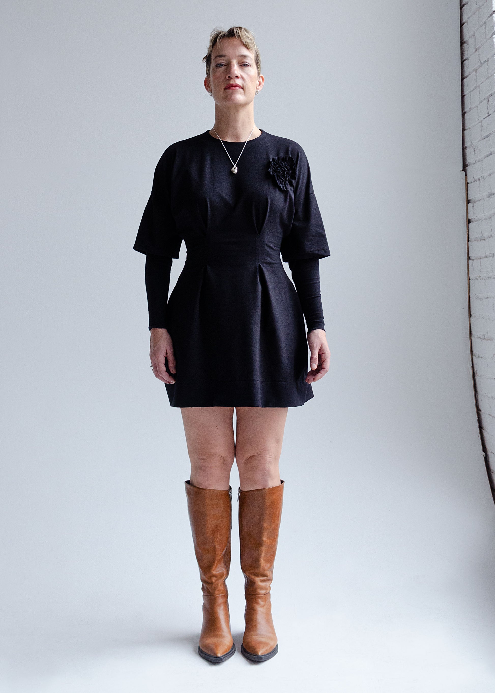 Front view, female model, drop shoulder, black knit mini dress with fit flare waist, double layer sleeve, appliqué flower detail at chest.
Cozy, stretchy  cotton spandex knit jersey fabric.Our version of the "Little Black Dress"