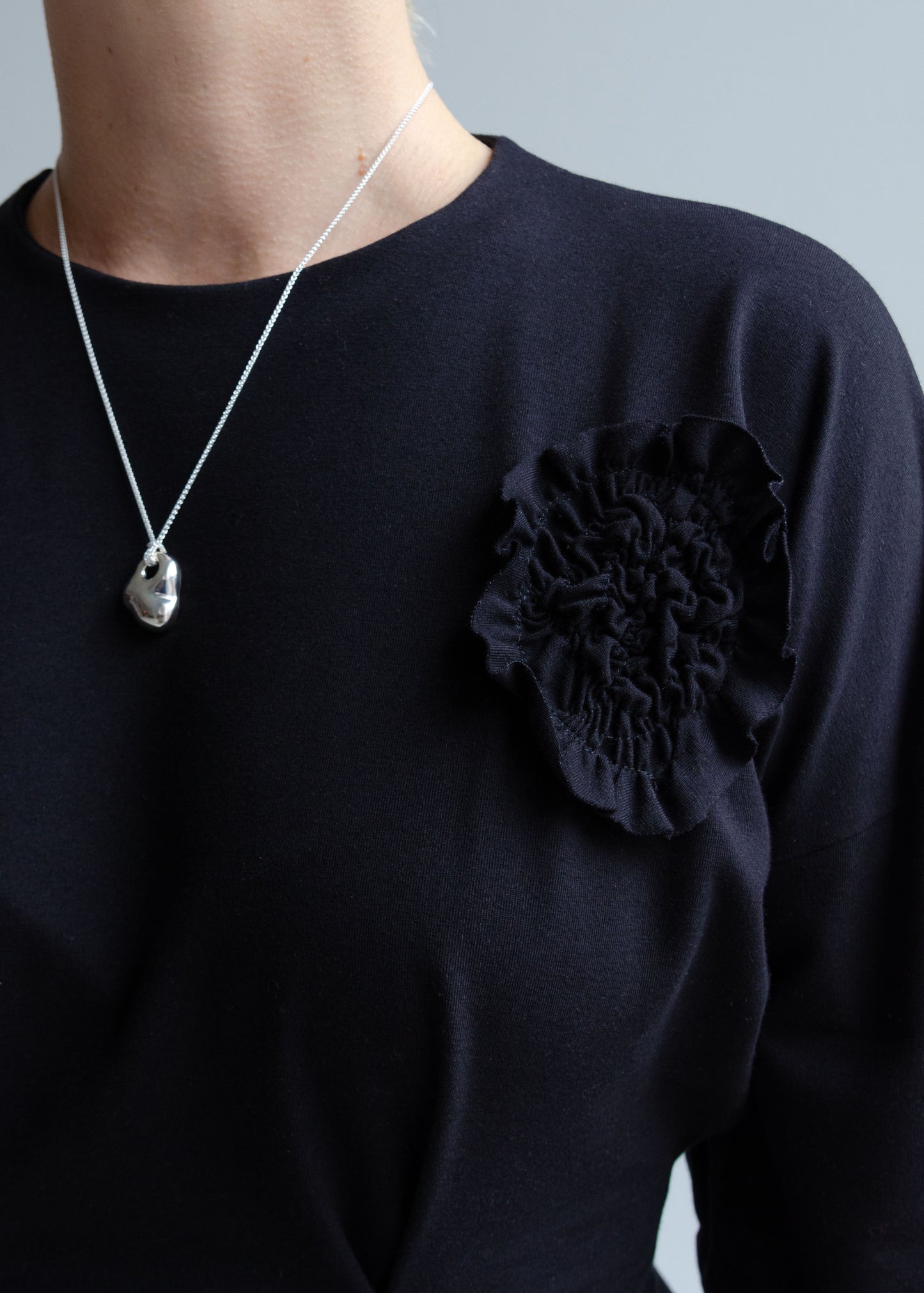Detail view, stretchy black knit cotton spandex jersey, flower appliqué detail, organic silver necklace around neck