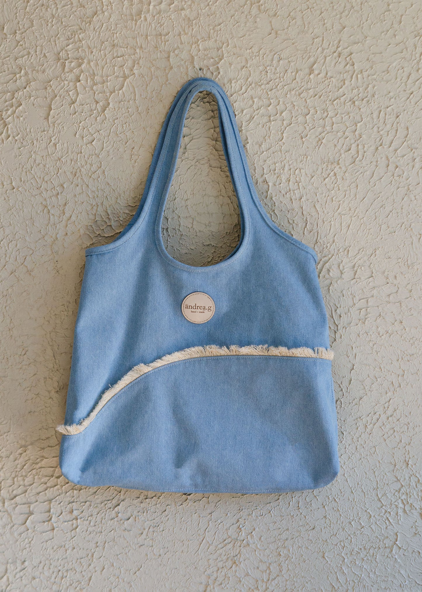 Mid-weight bleached denim tote bag with built-in shoulder straps, bound edges & curved seams with cotton fringe trim detailing. Laser-cut leather logo patch on the face side. Unlined.
This bag easily fits a laptop & sweater for those days when you're not quite sure what the weather will be like.