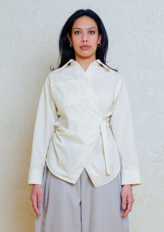 Cotton poplin shirt with asymmetrical front, adjustable waist closure with matte tortoiseshell print slider, gathering at waist side seams, shirt collar & patch pocket.Featuring an exaggerated baseball hem & back darts for a flattering, slightly fitted look.
Lightweight light yellow cotton poplin fabric features a subtle menswear-influenced stripe.