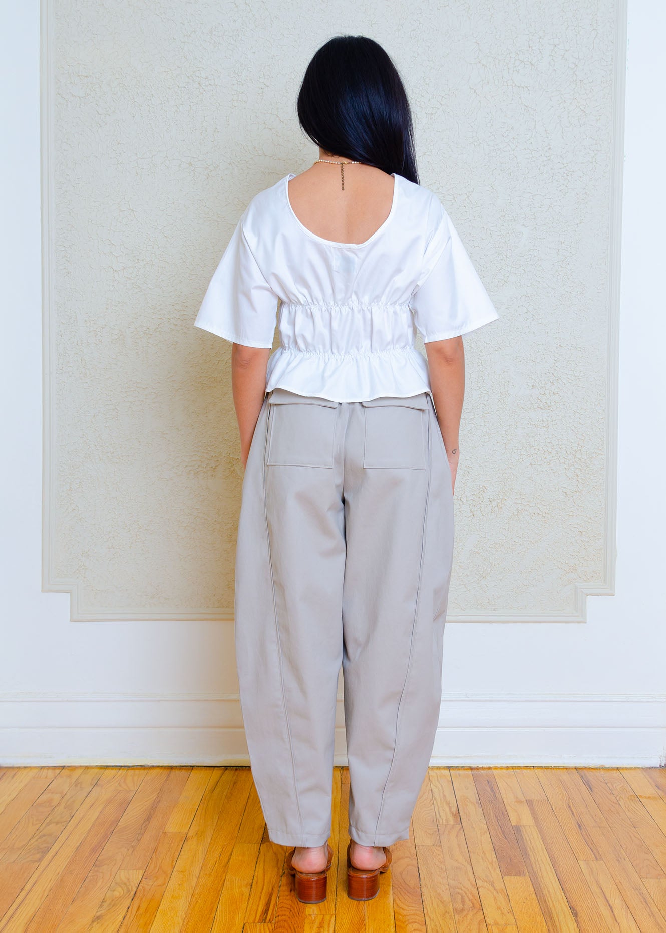 Full back view. Rouched short sleeve top with dropped shoulders and low back. Elasticized waist detailing allows for a greater size variation. Crisp cotton poplin fabric