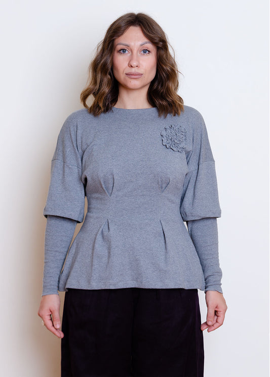 Cropped front view. Grey heather hip-length knit top with fit & flare waist, double layer sleeve appliqué flower detail at chest. Two large pleats at waist 
Cozy, stretchy organic cotton knit interlock fabric