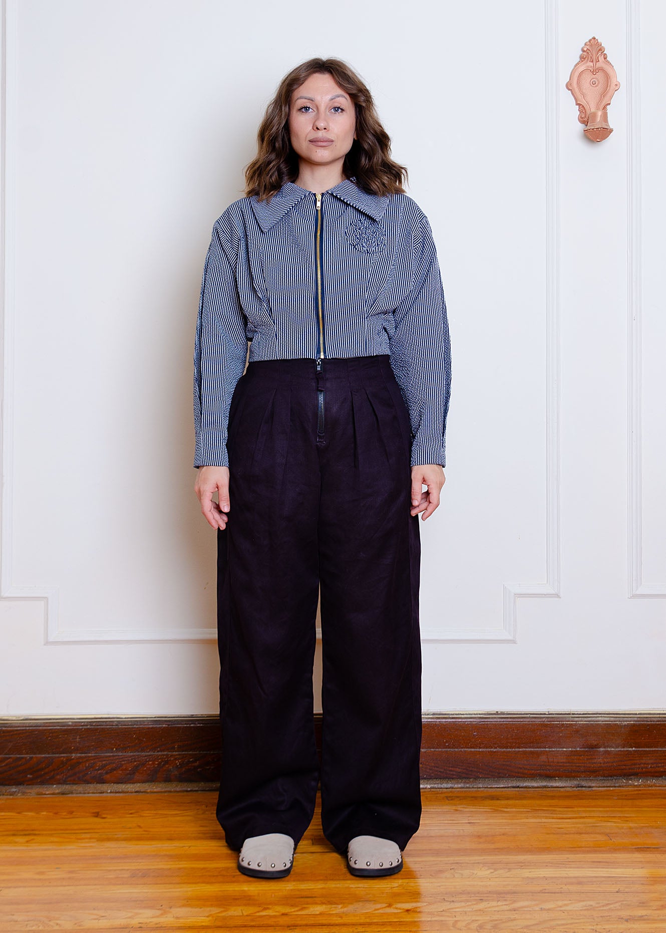 Full length front image on female model. Waist-length jacket with exposed zipper closure, oversized collar, floral appliqué detail at chest and box pleat detailing at waist and sleeves.
Jacket is fully lined with an inner patch pocket. 
Made from a beautiful classic navy and white pinstripe seersucker fabric
Jacket is styled with high waisted black pleated pants made from organic cotton and hemp twill fabric.