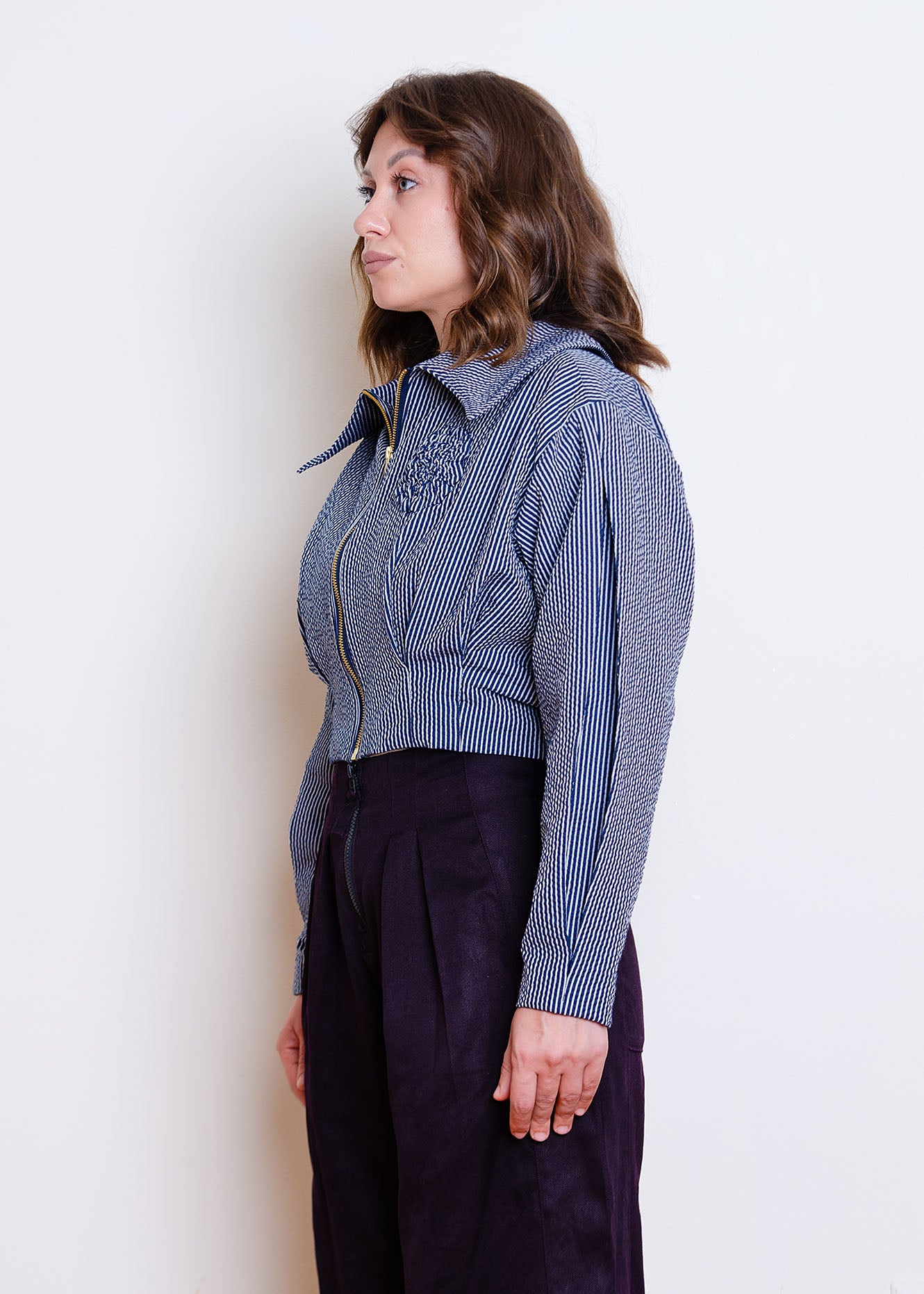 3/4 Cropped front image on female model. Waist-length jacket with exposed zipper closure, oversized collar, floral appliqué detail at chest and box pleat detailing at waist and sleeves.
Jacket is fully lined with an inner patch pocket.
Made from a beautiful classic navy and white pinstripe seersucker fabric
