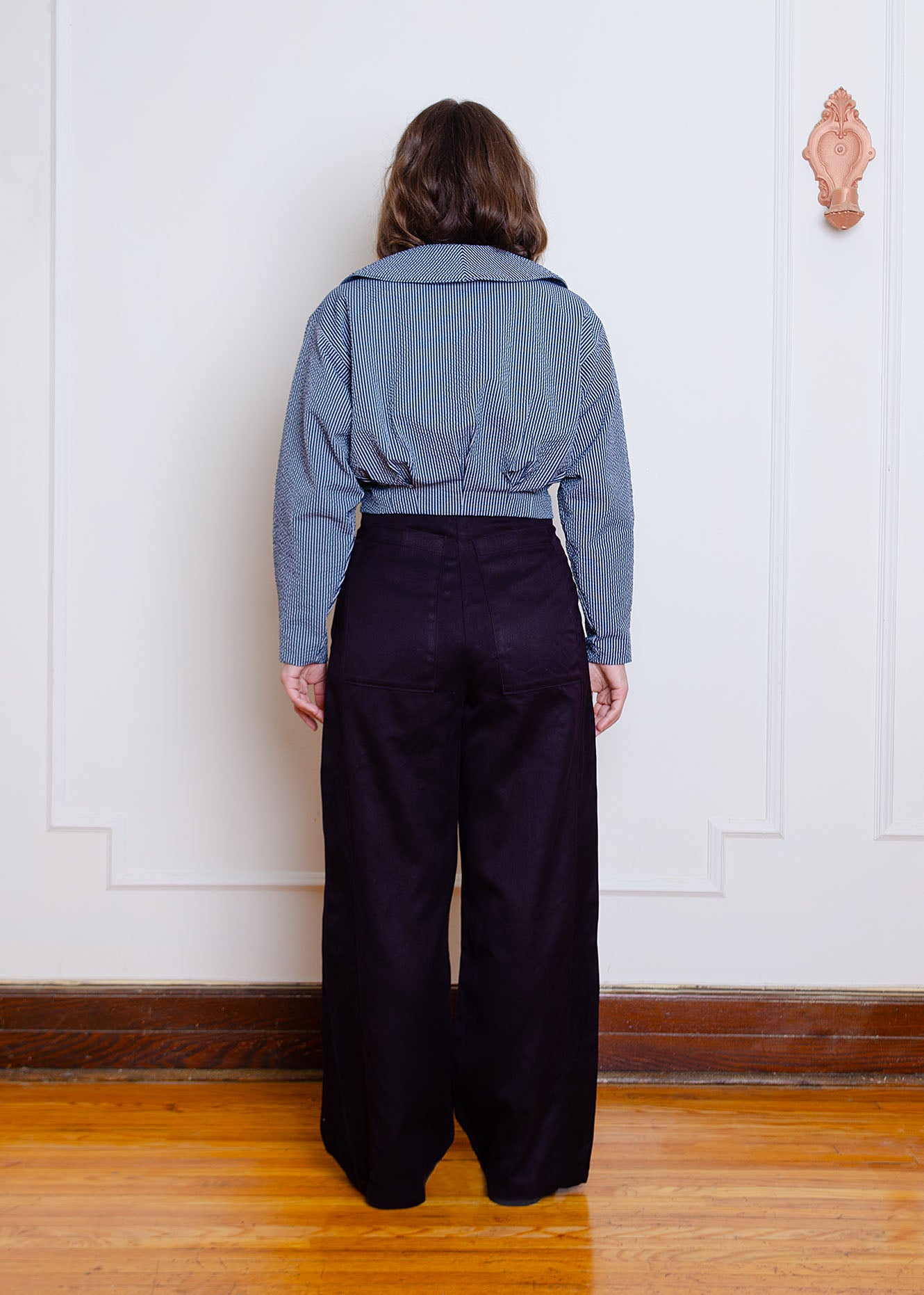 Full length back image on female model. Waist-length jacket with exposed zipper closure, oversized collar, floral appliqué detail at chest and box pleat detailing at waist and sleeves.
Jacket is fully lined with an inner patch pocket.
Made from a beautiful classic navy and white pinstripe seersucker fabric
Jacket is styled with high waisted black pleated pants made from organic cotton and hemp twill fabric.
