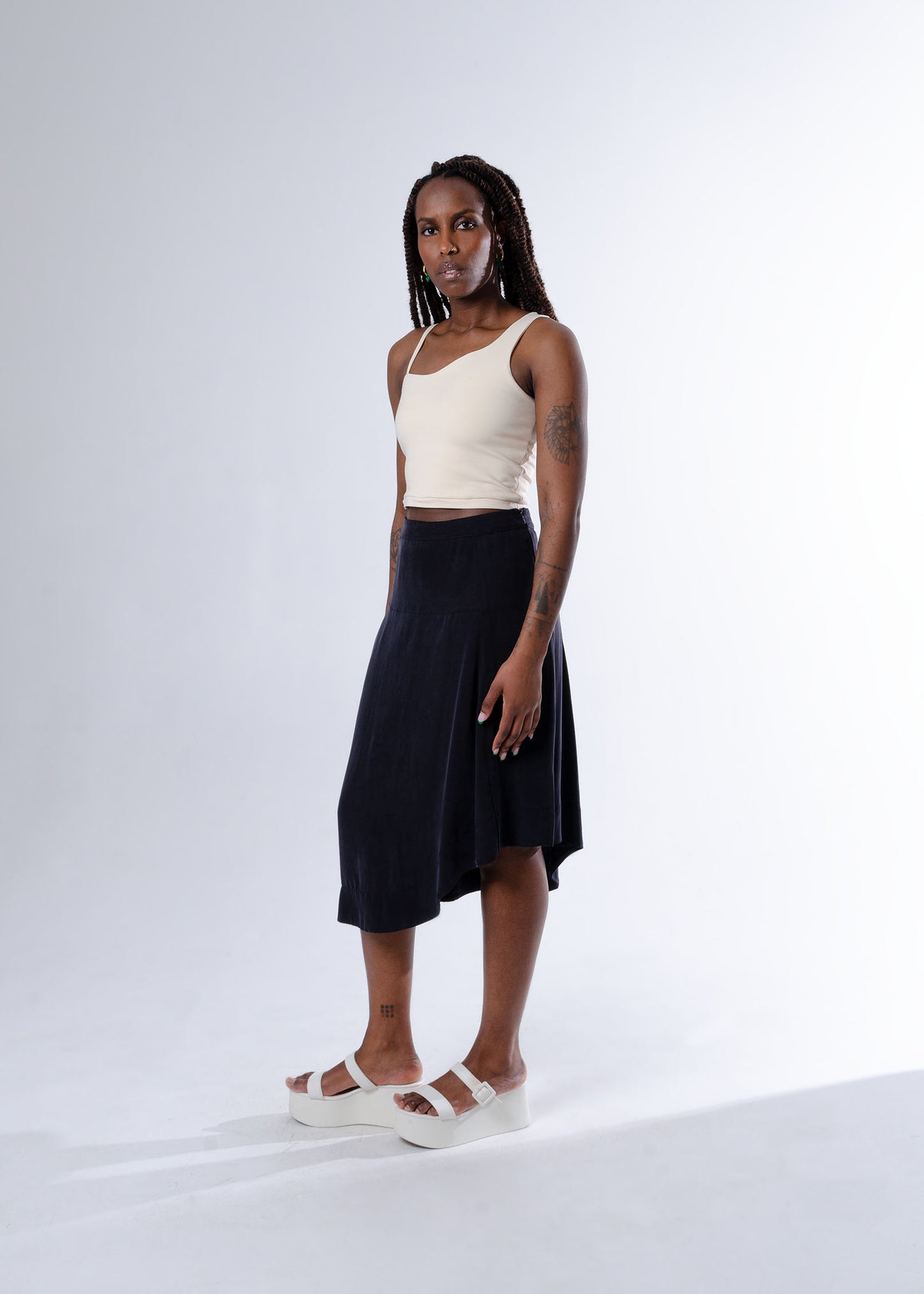 3/4 view of model wearing cream cotton cropped tank top with asymmetrical top edge and black midi skirt with asymmetrical wavy hem