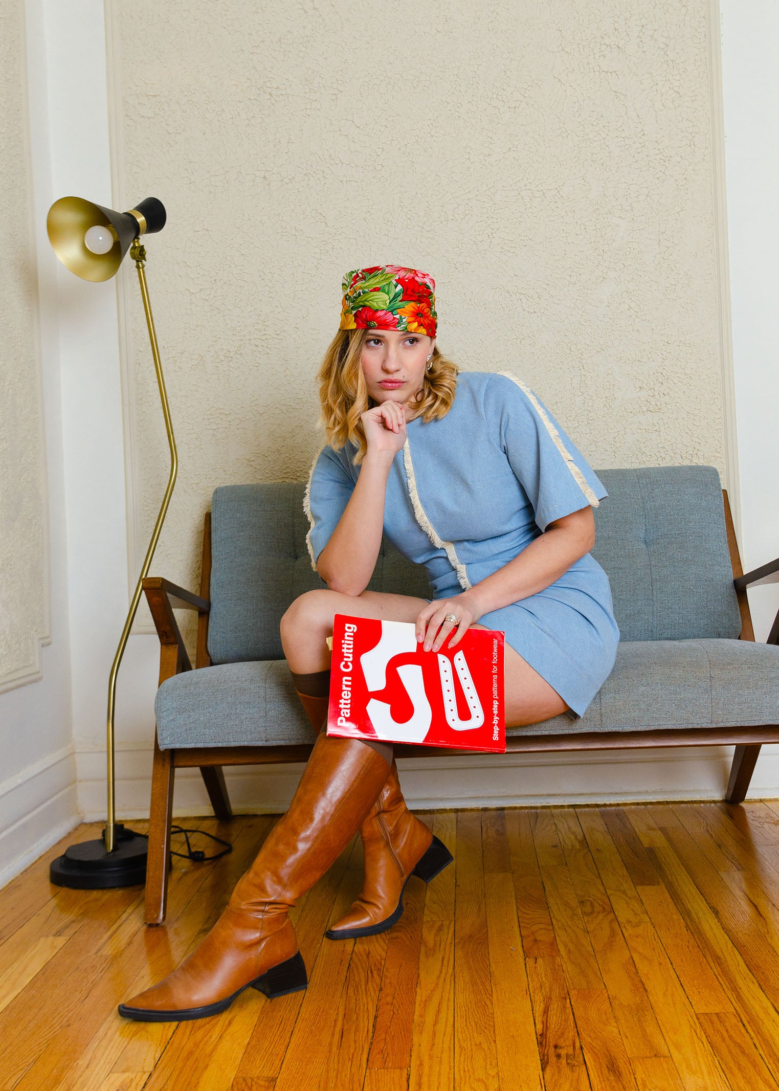 Fitted bleached denim mini dress with bust darts, rouched midsection. 100% cotton fringe trim detailing. Featuring slightly flared short sleeves that hit just above the elbow, low V back & back neck tie. Center back zip closure. Campaign image, styled with knee high camel coloured leather boots with pointy toe & block heel and an orange floral silk headscarf. 