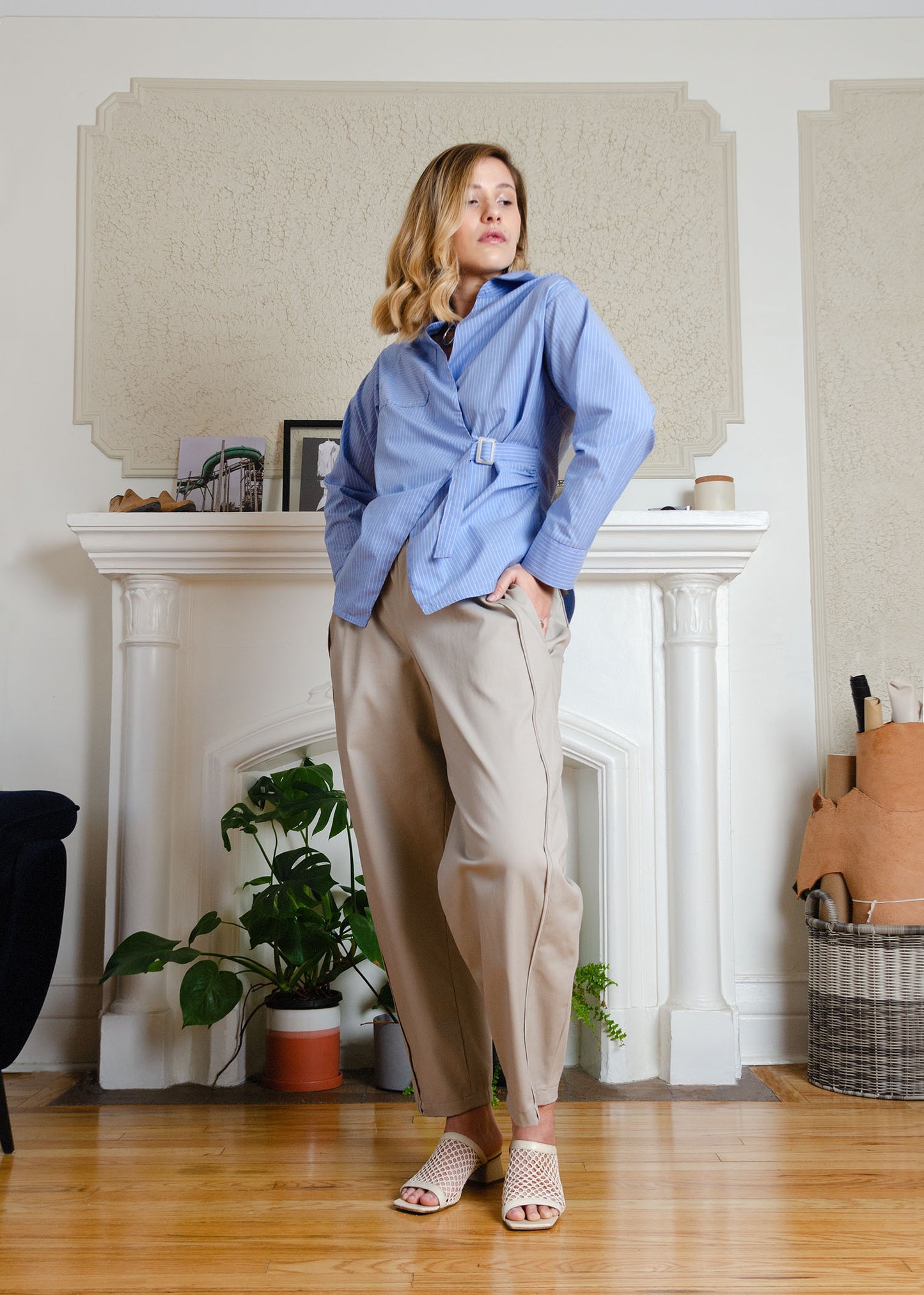 Front full view on model. Cotton poplin shirt with asymmetrical front, adjustable waist closure with matte tortoiseshell print slider, gathering at waist side seams, shirt collar & patch pocket.Featuring an exaggerated baseball hem & back darts for a flattering, slightly fitted look.

Lightweight cotton poplin fabric features a subtle menswear-influenced stripe 

Styled with beige barrel pants and cream mesh sandals