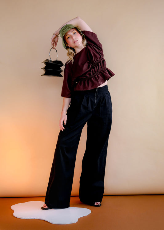 Blonde model wears chocolate brown tank top with two rows of elastic stitching at waist and high waisted black denim wide-leg pants with exposed centre front zipper